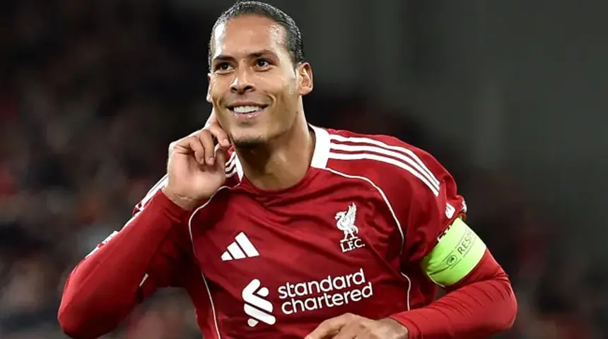 Liverpool FC player in a red jersey with captain's armband smiling on the pitch.