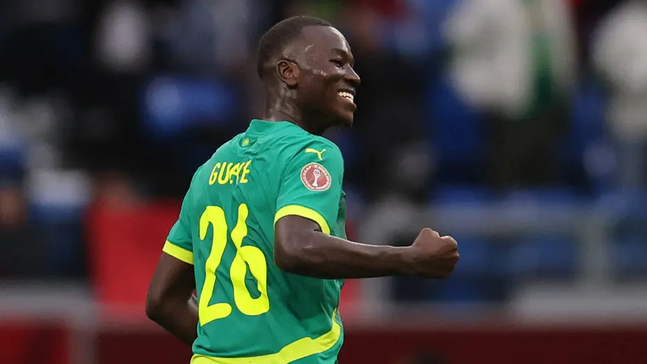 Soccer player in a green kit with yellow number 26 celebrating with a fist pump on the field.