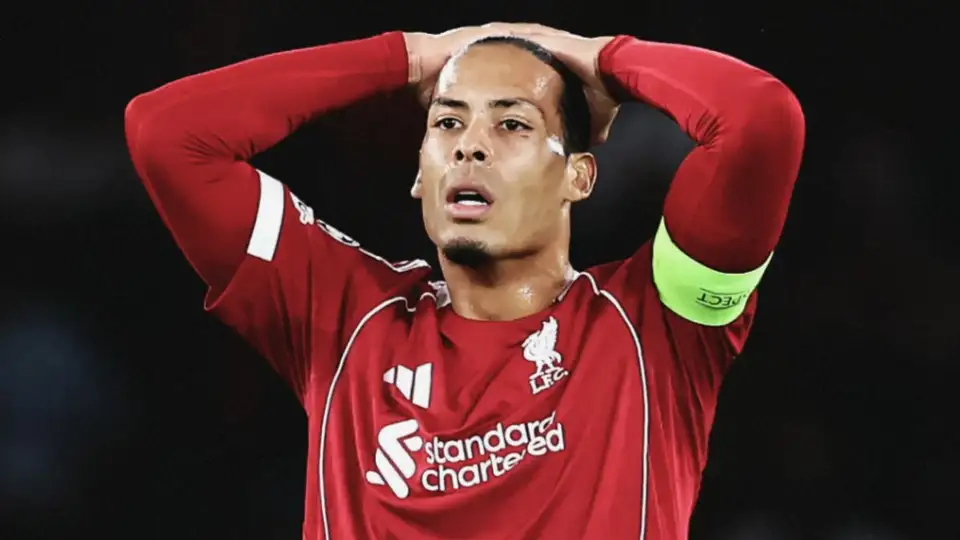 Footballer in a red Liverpool jersey with hands on head, wearing a green captain's armband, looking stressed at a match.
